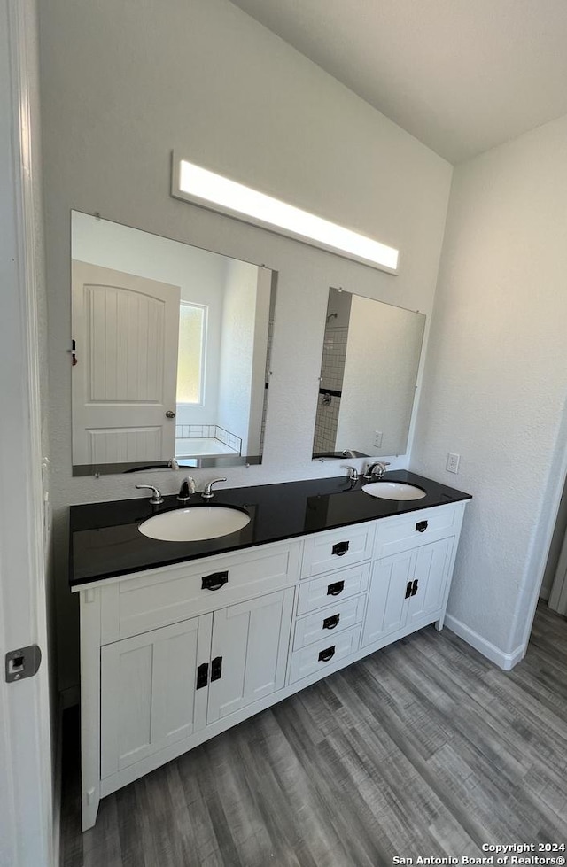 full bath with double vanity, wood finished floors, baseboards, and a sink