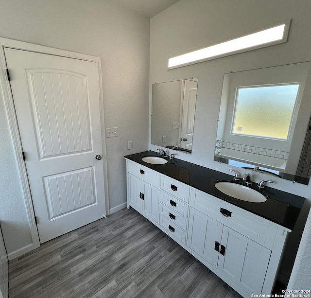 bathroom featuring a sink, baseboards, wood finished floors, and double vanity