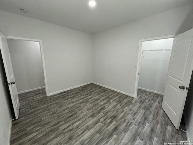 unfurnished bedroom with dark wood-type flooring, a spacious closet, baseboards, and a closet