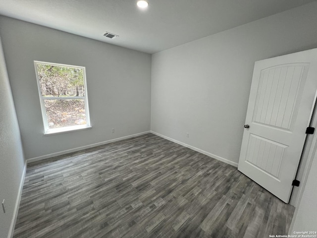 empty room featuring dark wood-style floors, visible vents, and baseboards