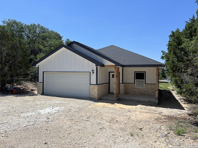 view of front of house with driveway, a garage, stone siding, and a shingled roof