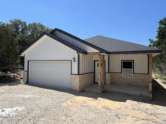 view of front of house featuring gravel driveway, a shingled roof, a garage, stone siding, and board and batten siding