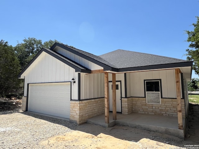 modern farmhouse with stone siding, board and batten siding, an attached garage, and a shingled roof