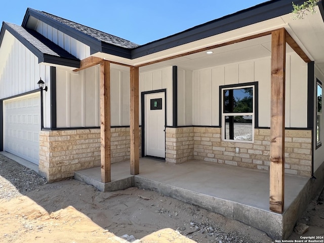 doorway to property featuring a garage, board and batten siding, stone siding, and a shingled roof