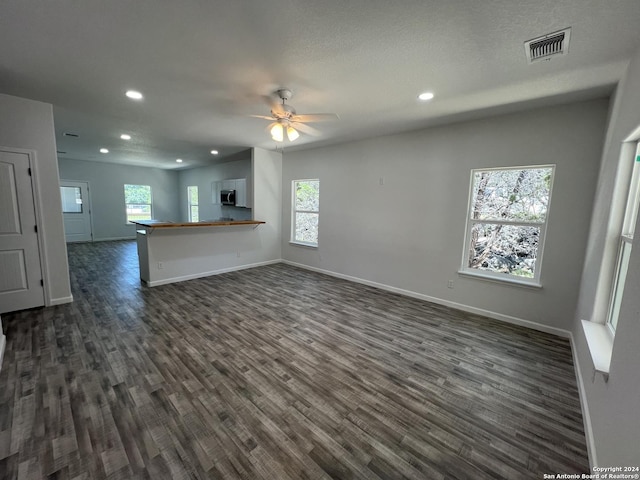 unfurnished living room featuring dark wood-style floors, visible vents, and plenty of natural light