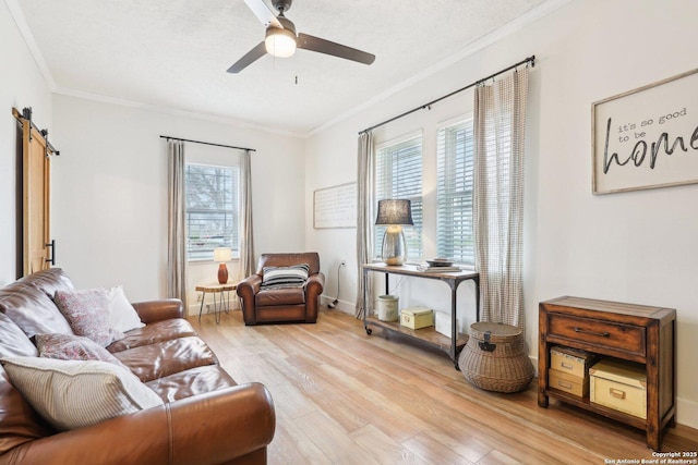 living area featuring a ceiling fan, baseboards, light wood finished floors, crown molding, and a barn door