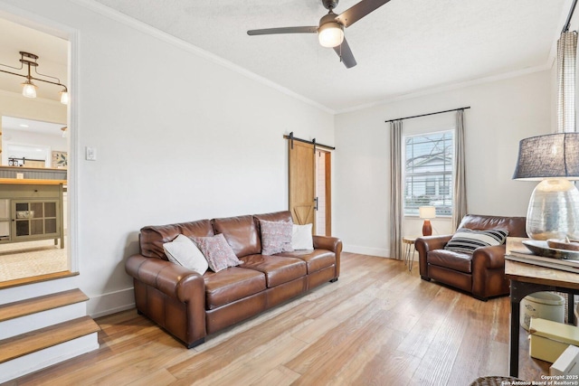 living room featuring baseboards, ceiling fan, a barn door, ornamental molding, and wood finished floors