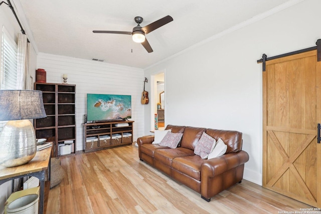 living room with light wood finished floors, visible vents, a barn door, and ornamental molding