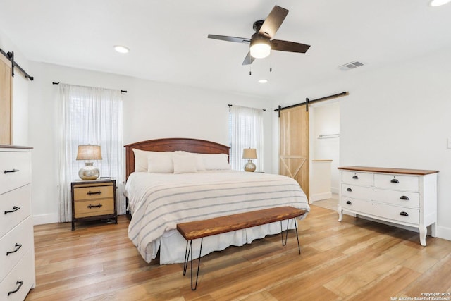 bedroom featuring a barn door, multiple windows, visible vents, and light wood finished floors