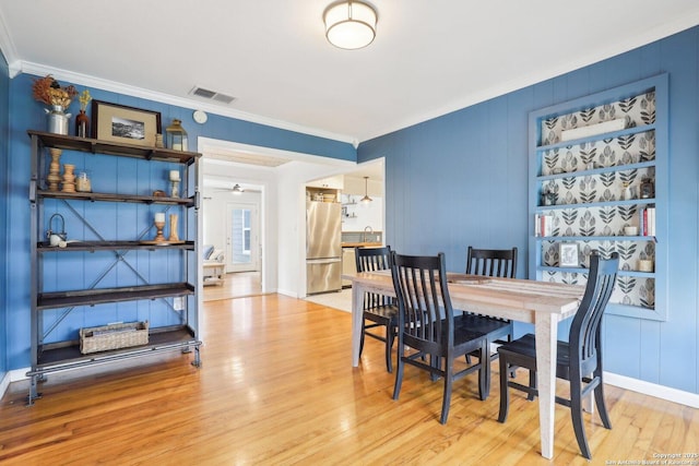 dining room with light wood-type flooring, visible vents, baseboards, and crown molding