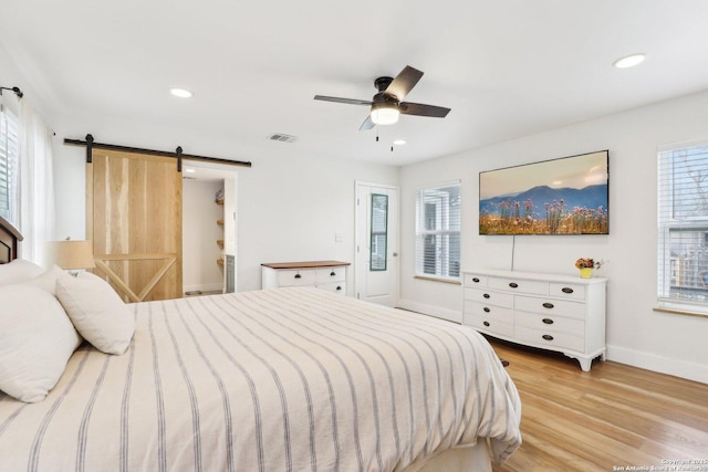 bedroom with recessed lighting, a barn door, visible vents, and light wood finished floors