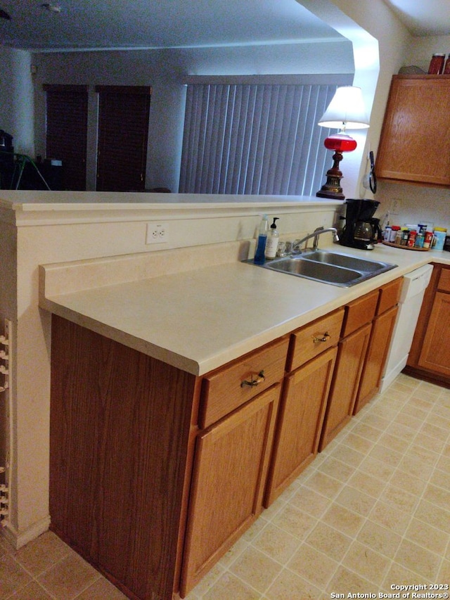 kitchen featuring brown cabinets, white dishwasher, light countertops, and a sink