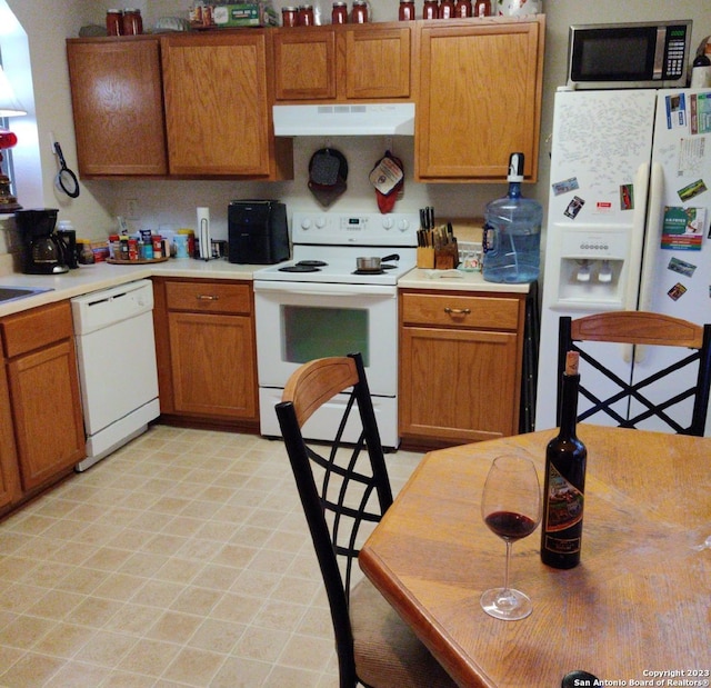 kitchen with brown cabinetry, white appliances, ventilation hood, and light countertops