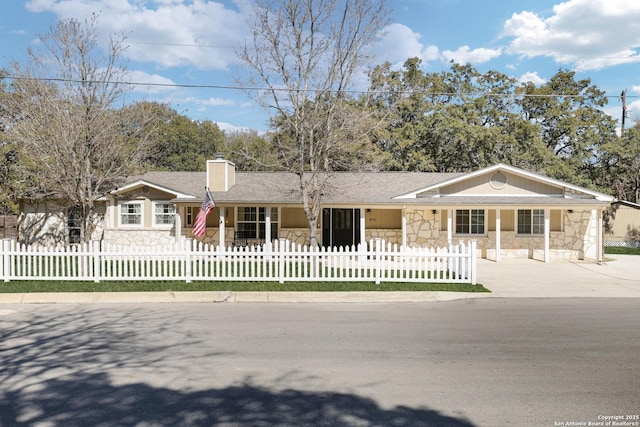 ranch-style house featuring a fenced front yard, concrete driveway, roof with shingles, a chimney, and stone siding