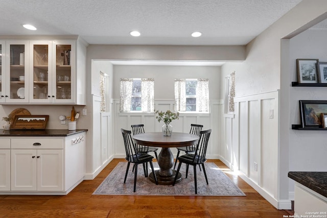 dining space featuring a textured ceiling, dark wood finished floors, and wainscoting