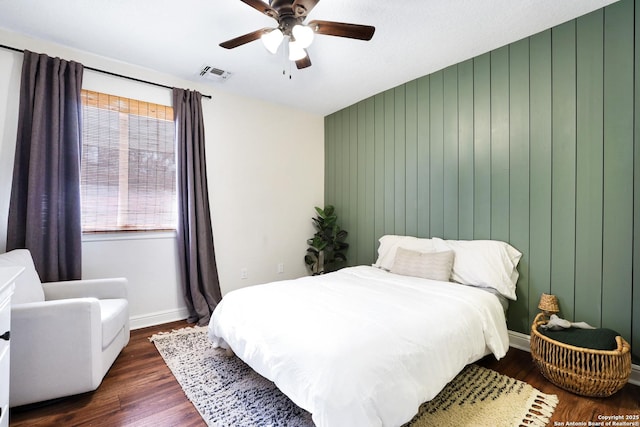 bedroom with visible vents, baseboards, ceiling fan, wood walls, and dark wood-style flooring