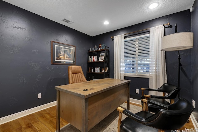 office space featuring a textured wall, visible vents, baseboards, and wood finished floors