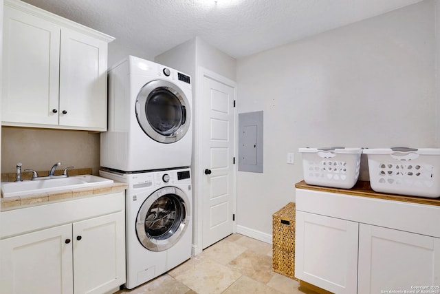 clothes washing area featuring stacked washer and dryer, a sink, electric panel, a textured ceiling, and cabinet space