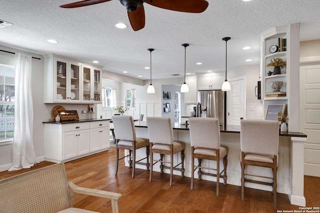 kitchen featuring light wood-style floors, stainless steel fridge, dark countertops, and a breakfast bar area