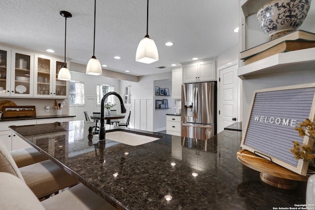 kitchen featuring a kitchen bar, a sink, stainless steel fridge with ice dispenser, glass insert cabinets, and hanging light fixtures