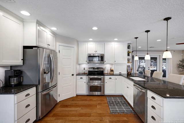 kitchen with appliances with stainless steel finishes, a peninsula, wood finished floors, white cabinets, and a sink