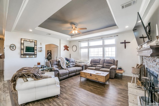 living room featuring a tray ceiling, wood finished floors, visible vents, and arched walkways