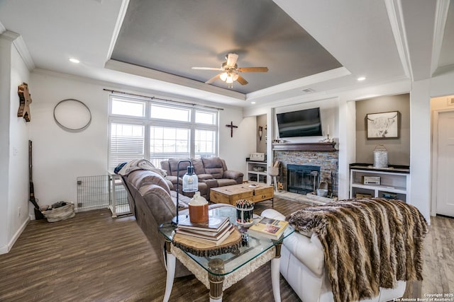 living room featuring ornamental molding, a ceiling fan, wood finished floors, a stone fireplace, and a raised ceiling