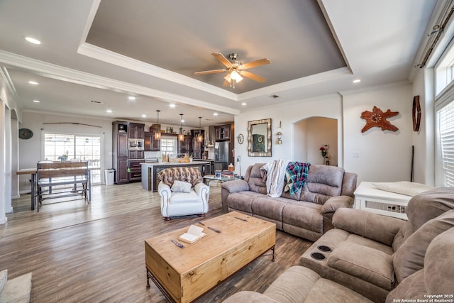 living room featuring ceiling fan, a tray ceiling, recessed lighting, wood finished floors, and arched walkways