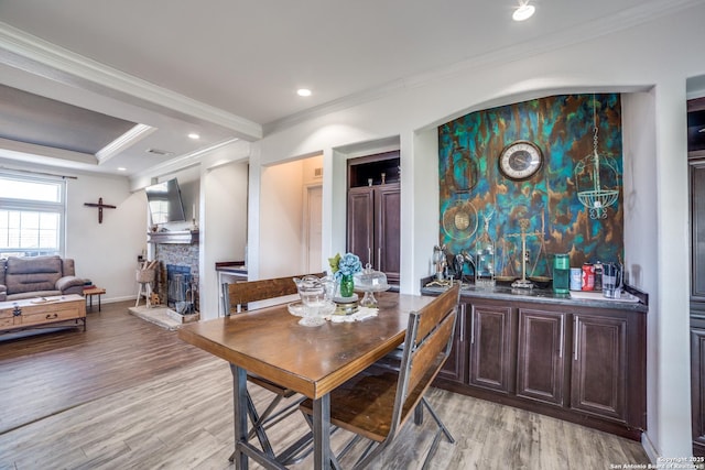 dining area with a stone fireplace, crown molding, light wood-style floors, and a tray ceiling