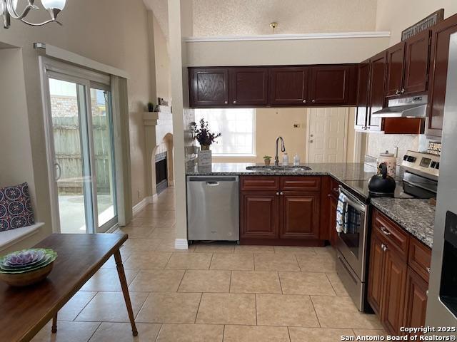 kitchen featuring dark stone countertops, a sink, under cabinet range hood, appliances with stainless steel finishes, and backsplash