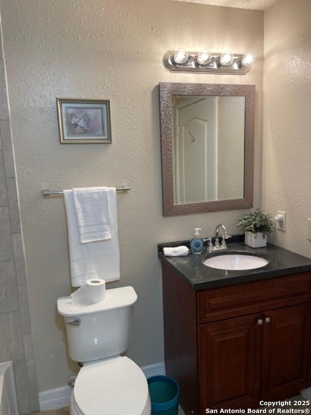 full bathroom with baseboards, toilet, a textured wall, a bath, and vanity