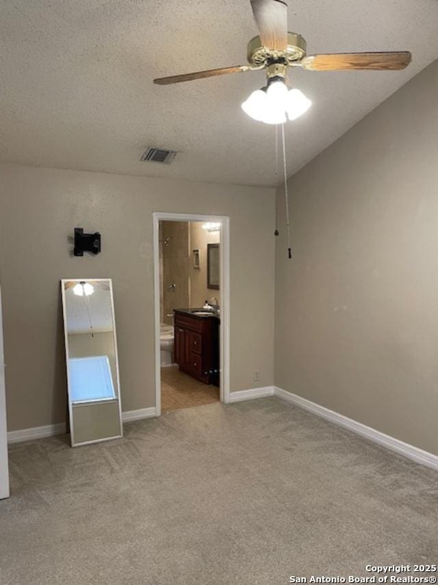 unfurnished bedroom featuring baseboards, visible vents, ensuite bath, a textured ceiling, and light colored carpet