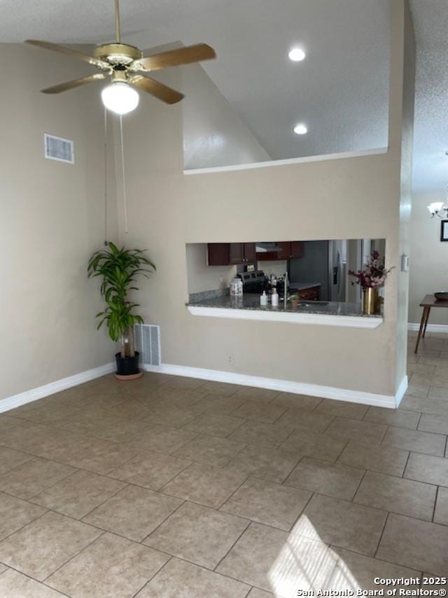 unfurnished living room with visible vents, ceiling fan with notable chandelier, high vaulted ceiling, and baseboards