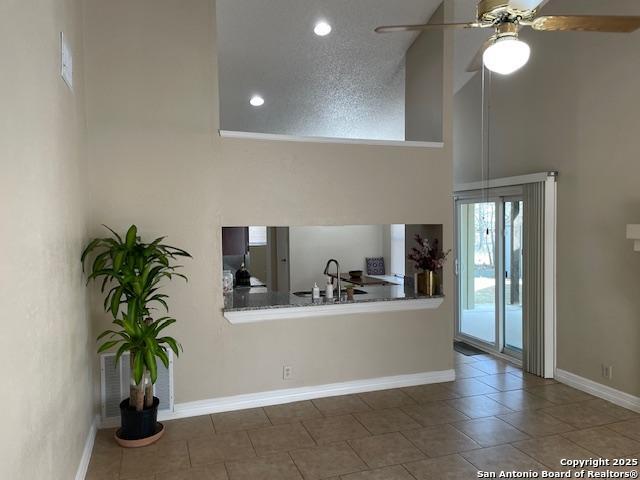 kitchen with tile patterned floors, a ceiling fan, a sink, a high ceiling, and baseboards