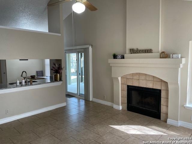 unfurnished living room featuring high vaulted ceiling, a ceiling fan, a sink, baseboards, and a tile fireplace