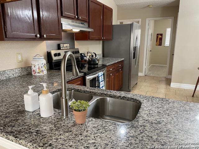 kitchen with stone counters, a sink, stainless steel appliances, dark brown cabinets, and under cabinet range hood