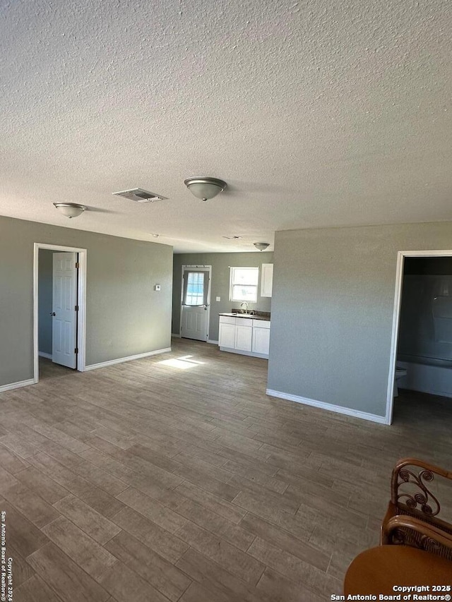 unfurnished living room featuring a sink, baseboards, visible vents, and wood finished floors