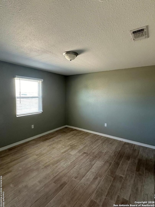 empty room with dark wood-type flooring, baseboards, visible vents, and a textured ceiling