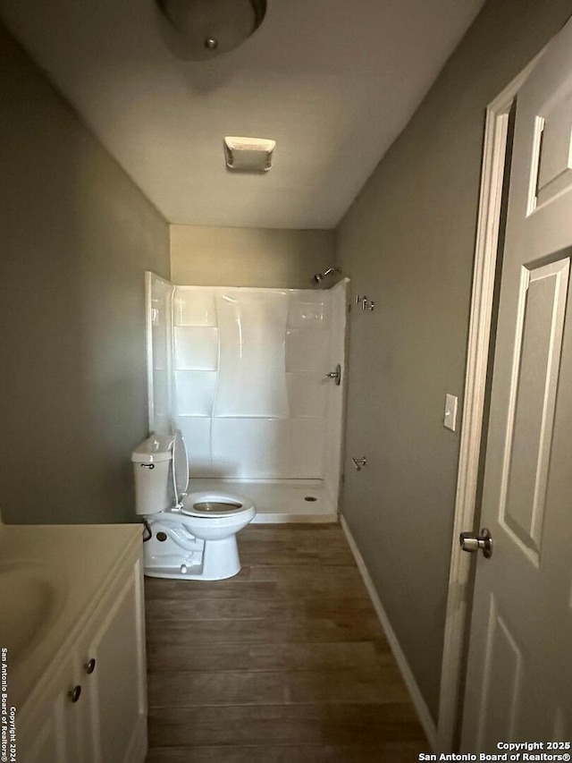 bathroom featuring vanity, wood finished floors, baseboards, a shower, and toilet