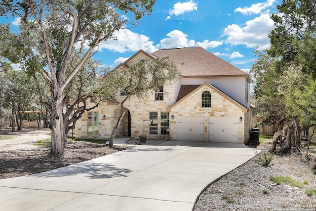 french country inspired facade with stone siding, cooling unit, concrete driveway, and a shingled roof