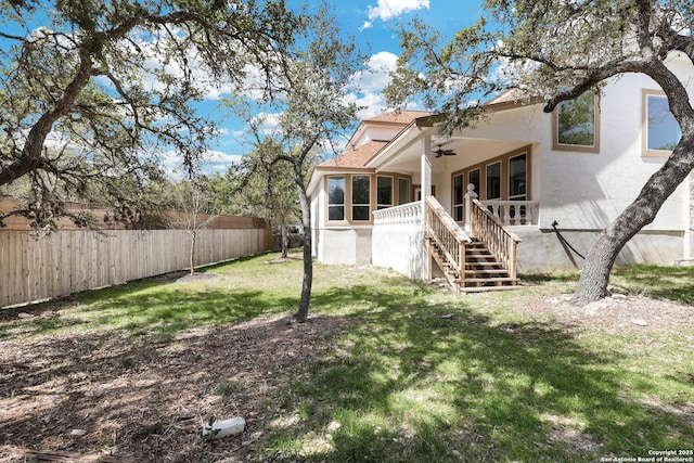 rear view of property featuring stairway, fence, a ceiling fan, stucco siding, and a lawn