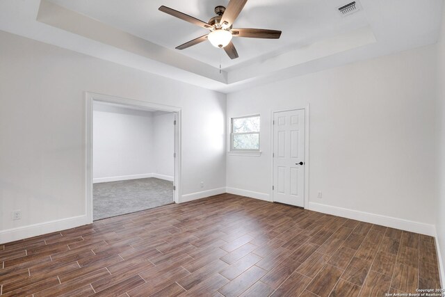 spare room featuring dark wood finished floors, a tray ceiling, baseboards, and visible vents