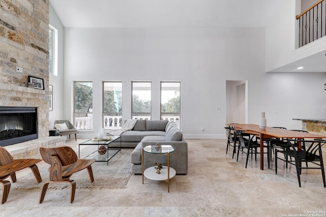 living room featuring a stone fireplace, baseboards, and a towering ceiling