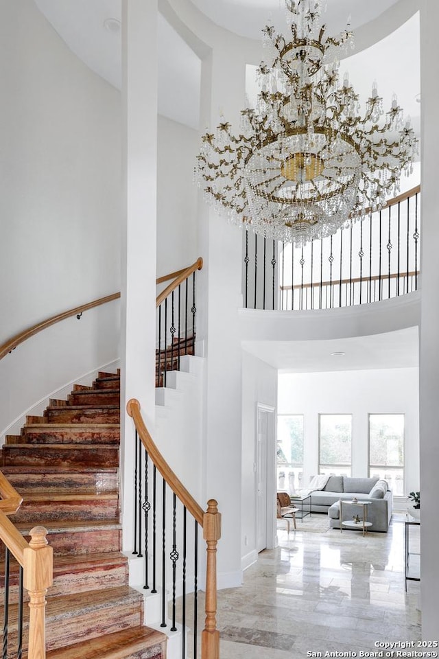 stairway featuring marble finish floor, baseboards, an inviting chandelier, and a towering ceiling