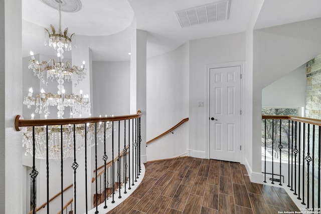 corridor featuring baseboards, visible vents, wood tiled floor, a notable chandelier, and an upstairs landing