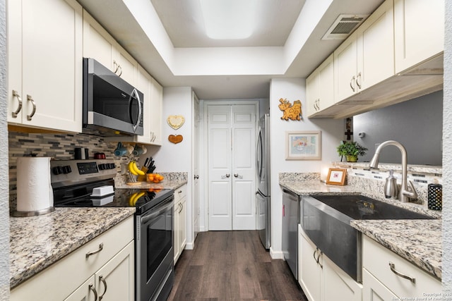 kitchen with visible vents, a sink, a tray ceiling, stainless steel appliances, and decorative backsplash