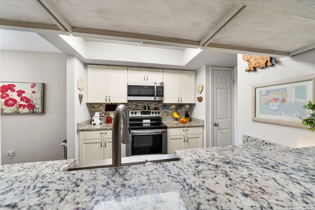 kitchen featuring tasteful backsplash, white cabinetry, stainless steel appliances, and light stone countertops