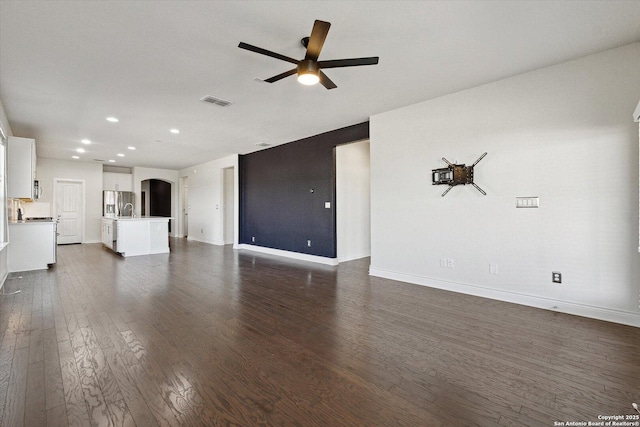 unfurnished living room with a ceiling fan, baseboards, dark wood finished floors, arched walkways, and a sink