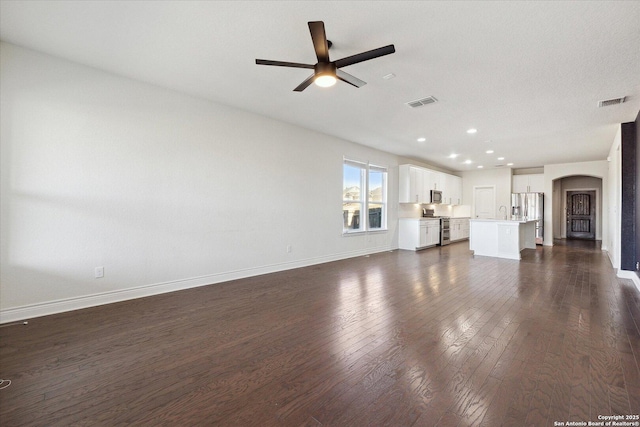 unfurnished living room featuring a ceiling fan, baseboards, dark wood finished floors, recessed lighting, and arched walkways