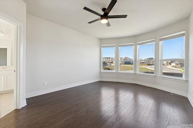 empty room with baseboards, a healthy amount of sunlight, dark wood finished floors, and a ceiling fan